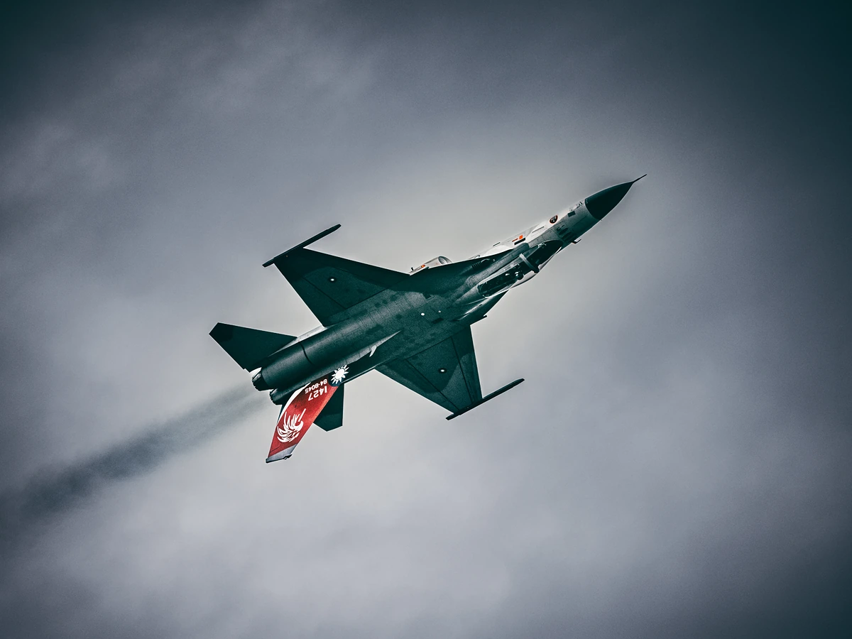 The same red-tailed fighter banks overhead, showing its underside, a thin smoke trail behind.