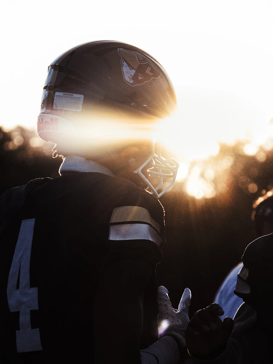 A football player seen from behind in near-silhouette, low sun flaring through his helmet.