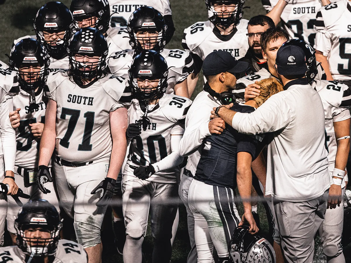 Coaches wrap their arms around a player as teammates in white jerseys look on.