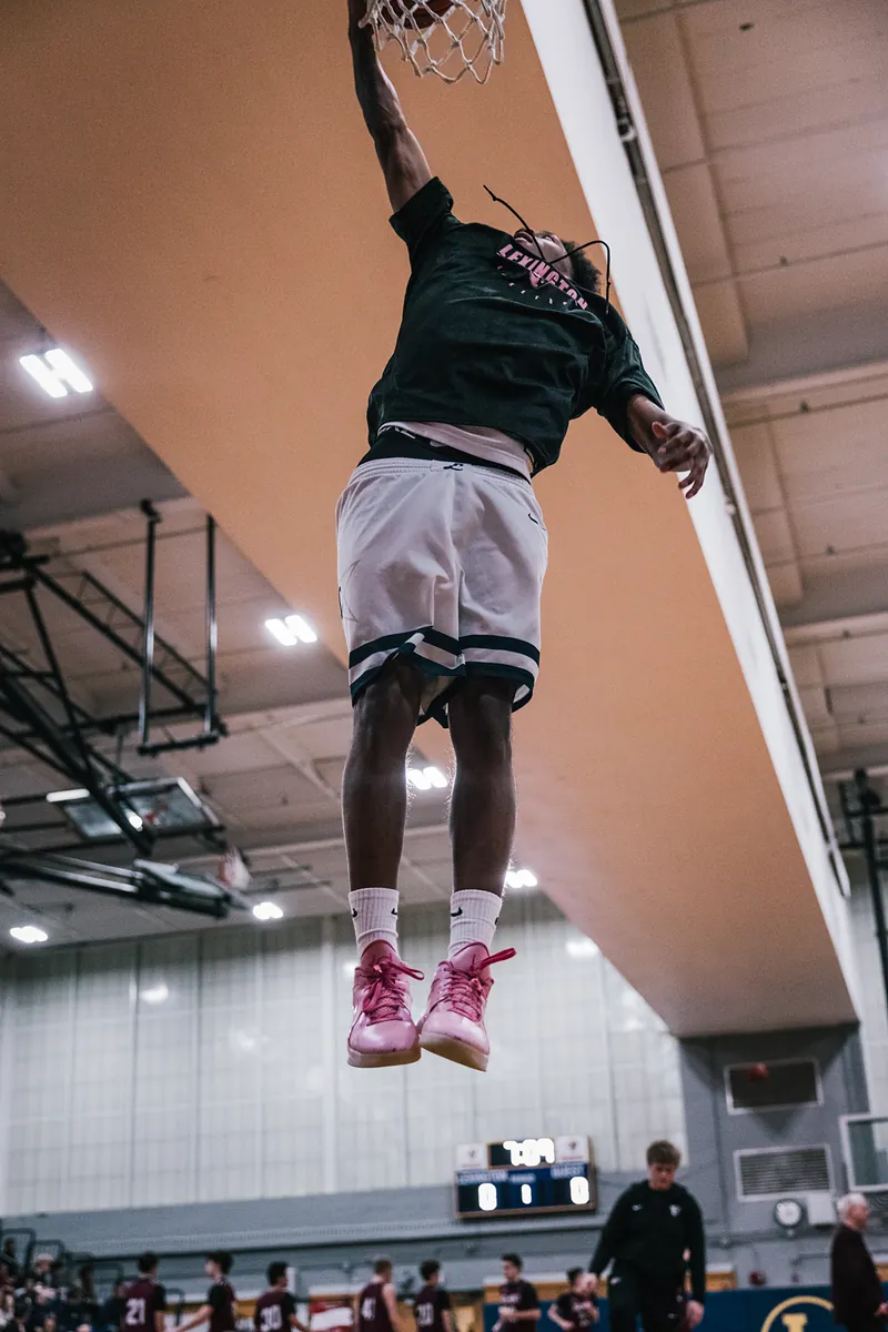Low-angle view of a player in pink shoes hanging on the rim during warm-ups.