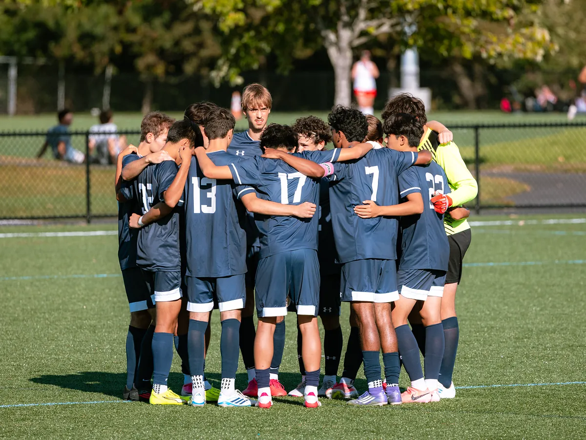 A soccer team in navy kits huddles on the field.
