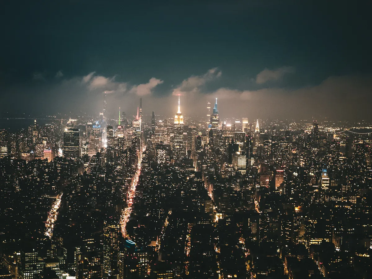 Manhattan at night from high above, avenues streaked with traffic and the Empire State Building in the haze.